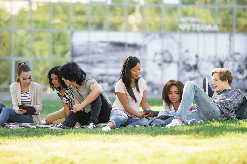 Group of diverse college students reading on an outdoor grassy area
